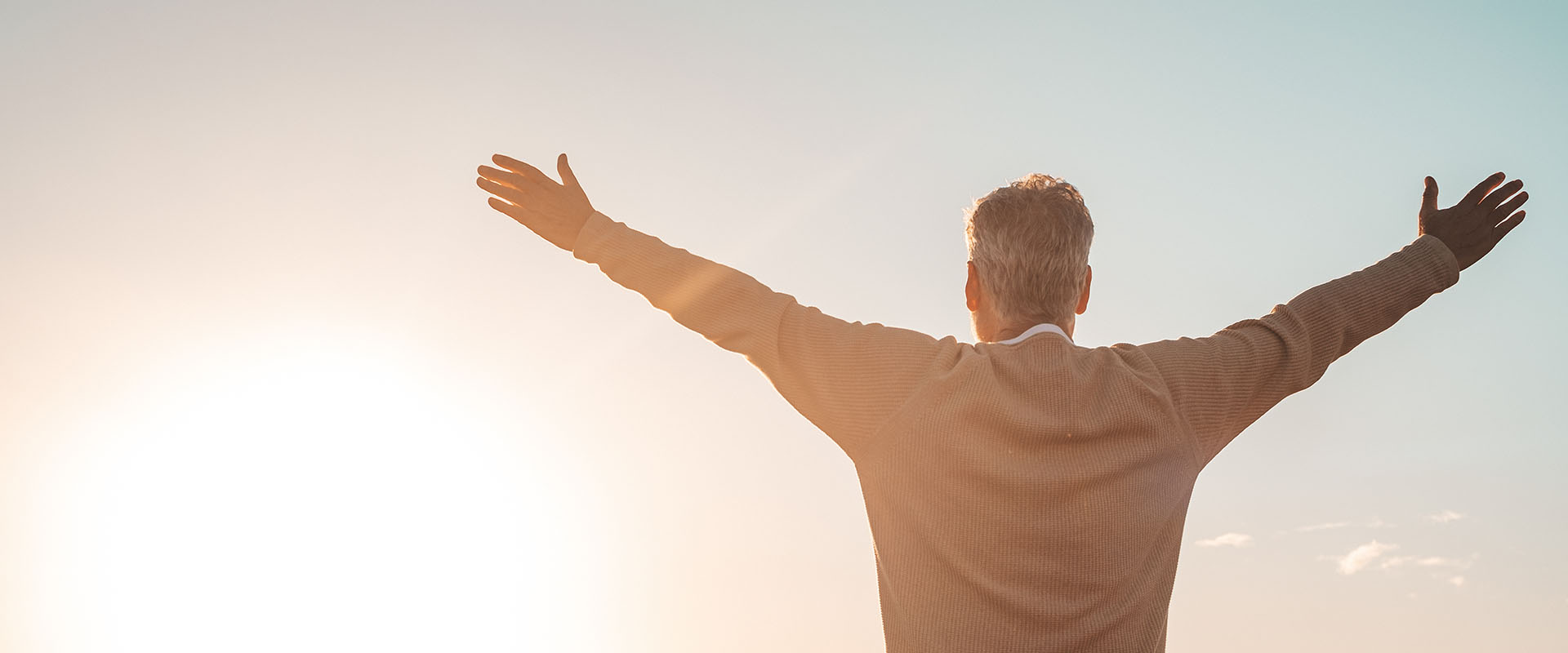 Older gentleman with outstretched arms watching sunset